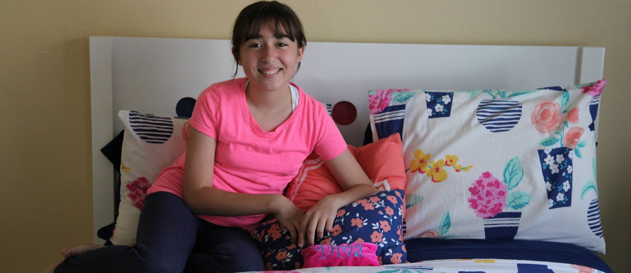 Dana sitting on her bed at home.